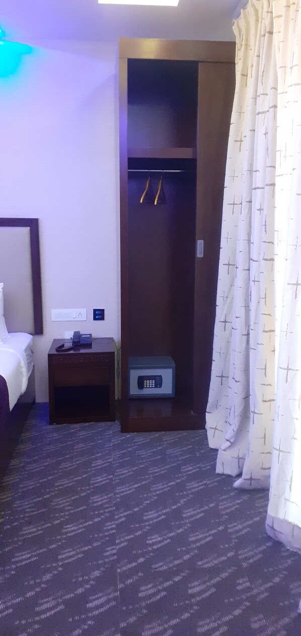 Habitación de hotel con cama, una mesita de noche con teléfono y control remoto, un armario con espejo y una cortina con estampado cruzado.
