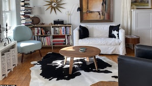 A living room with a white sofa, a cowhide rug, a bookshelf, and a star-shaped wall decoration. - Chic Farmhse Cottage, private  beach, WiFi unlimited streaming/zoom, A/C, 600sf (Blue Hill)