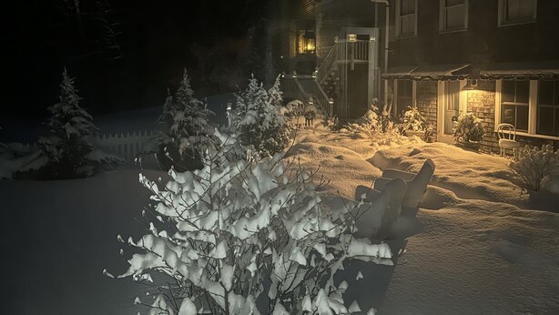 A snow-covered landscape with a house featuring a porch and a lit entrance. - Chic Farmhse Cottage, private  beach, WiFi unlimited streaming/zoom, A/C, 600sf (Blue Hill)