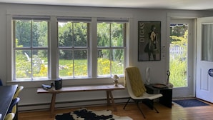 A room with large windows, a wooden desk, a chair, a cowhide rug, and a door leading outside. - Chic Farmhse Cottage, private  beach, WiFi unlimited streaming/zoom, A/C, 600sf (Blue Hill)