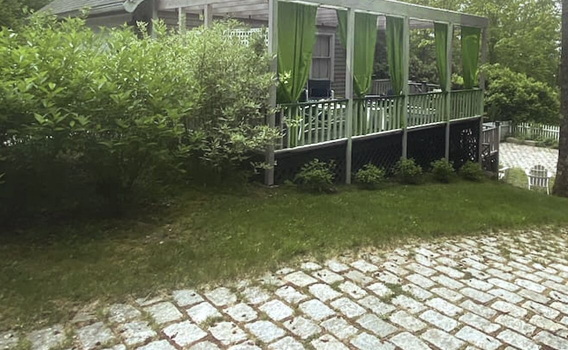 Eine überdachte Veranda mit grünen Vorhängen, einem Steinweg und üppiger Bepflanzung.