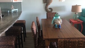Un comedor con mesa de madera y sillas de mimbre, una araña y un adorno de caballito de mar en la pared.