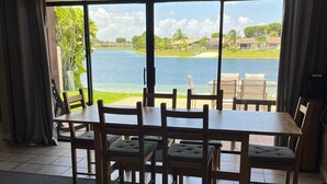 Un espace repas comprenant une grande table et des chaises, une vue sur un lac et un patio avec une piscine.