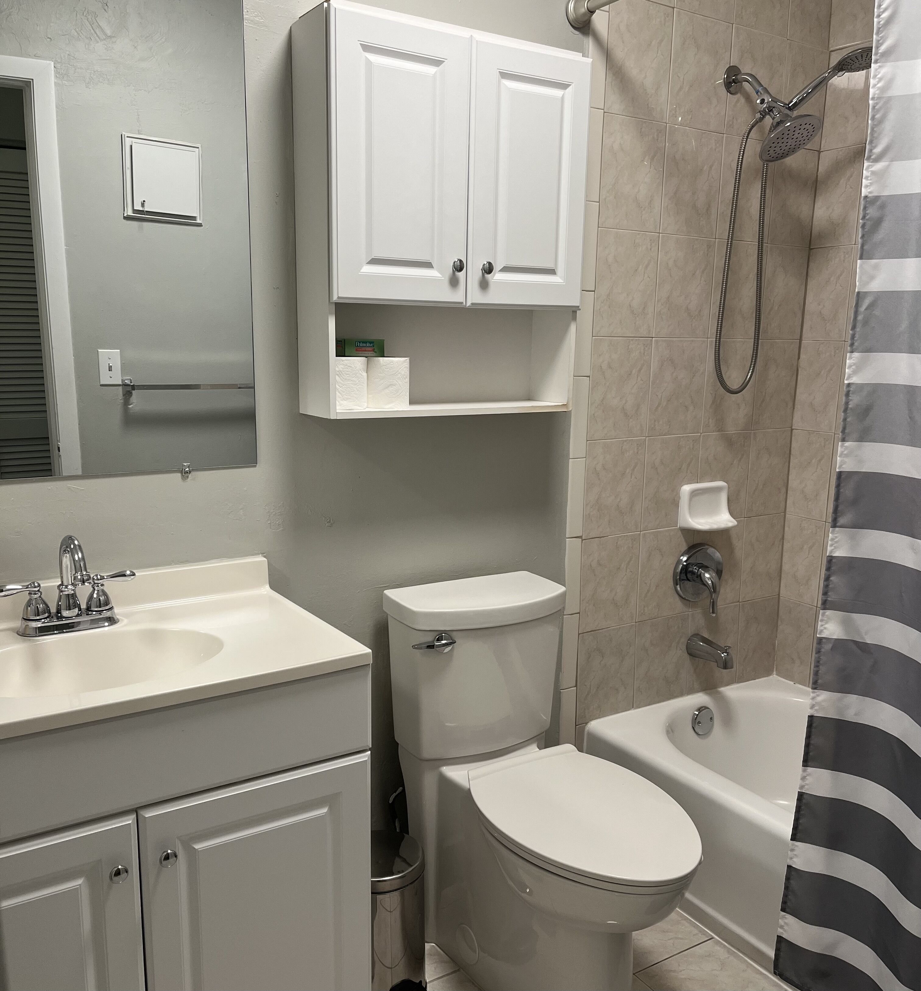 A bathroom with a toilet, sink, and bathtub. There are cabinets above the sink and a showerhead above the bathtub.