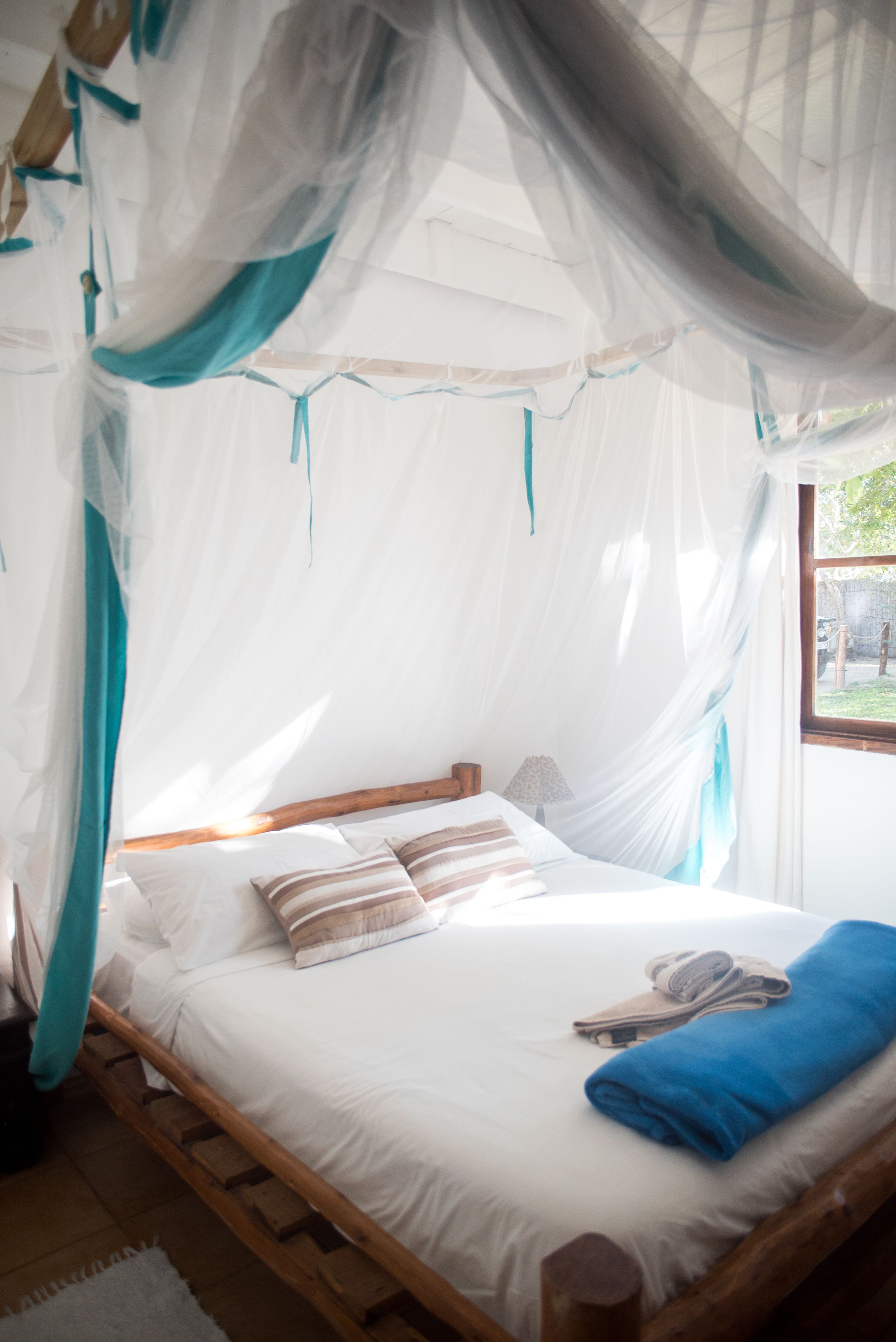 Una cama con estructura de madera, ropa de cama blanca y una manta azul.