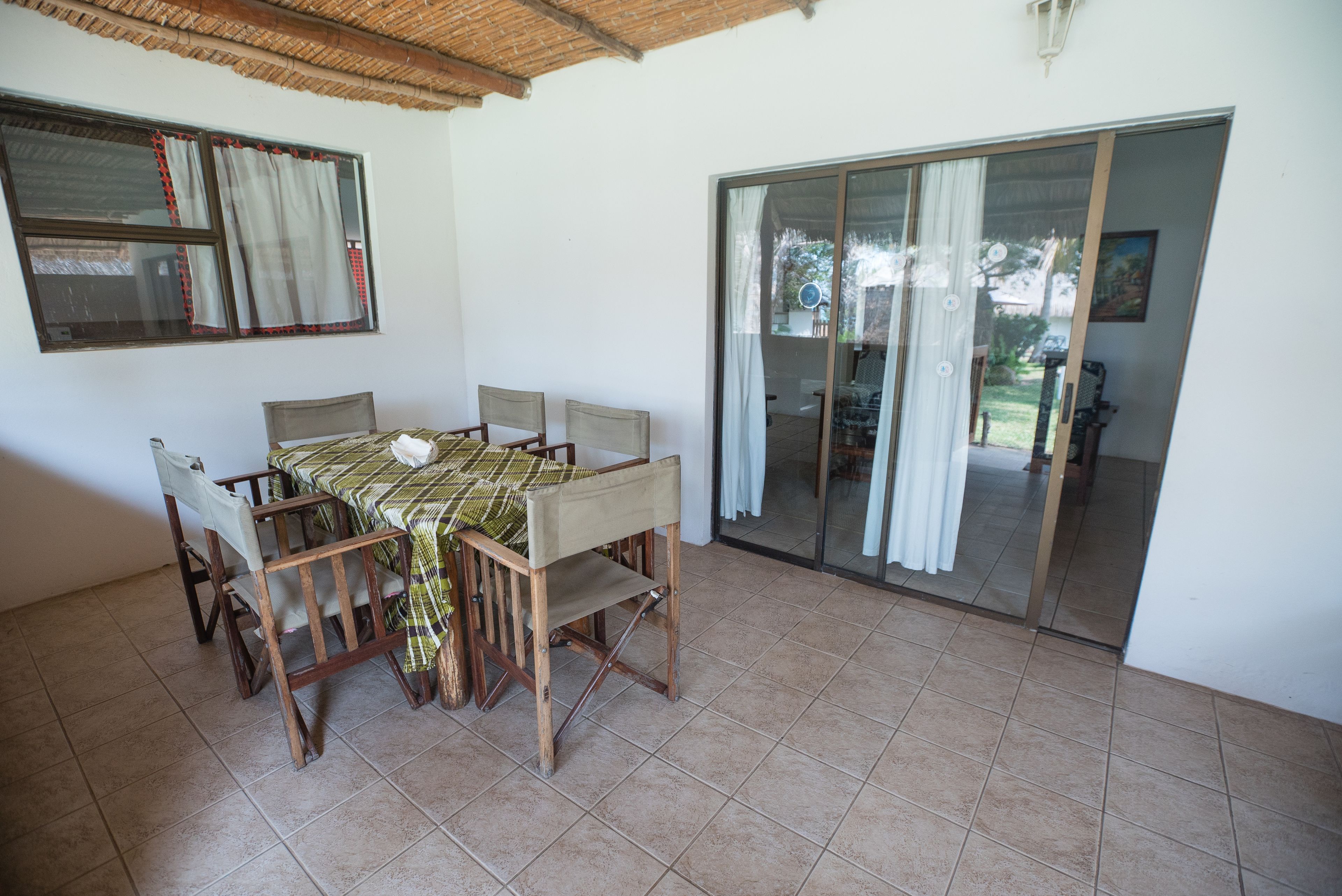 Un comedor con mesa y sillas, una ventana con cortinas y un puerta corrediza de vidrio que da a un espacio exterior.
