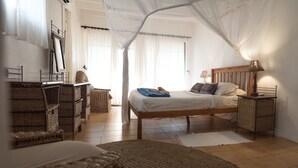 Een slaapkamer met een houten bed, nachtkastje, rieten meubels en een hemelbed.