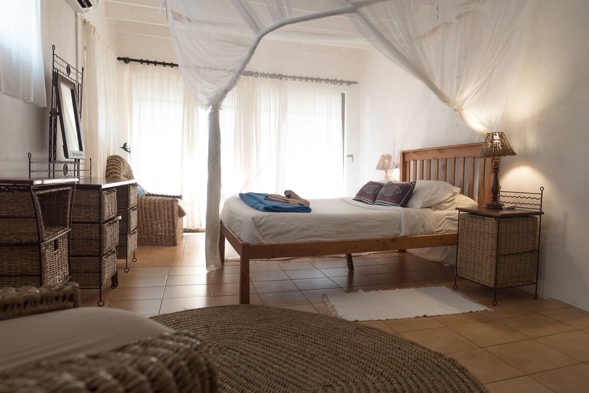 A bedroom with a wooden bed, a nightstand, wicker furniture, and a canopy bed.