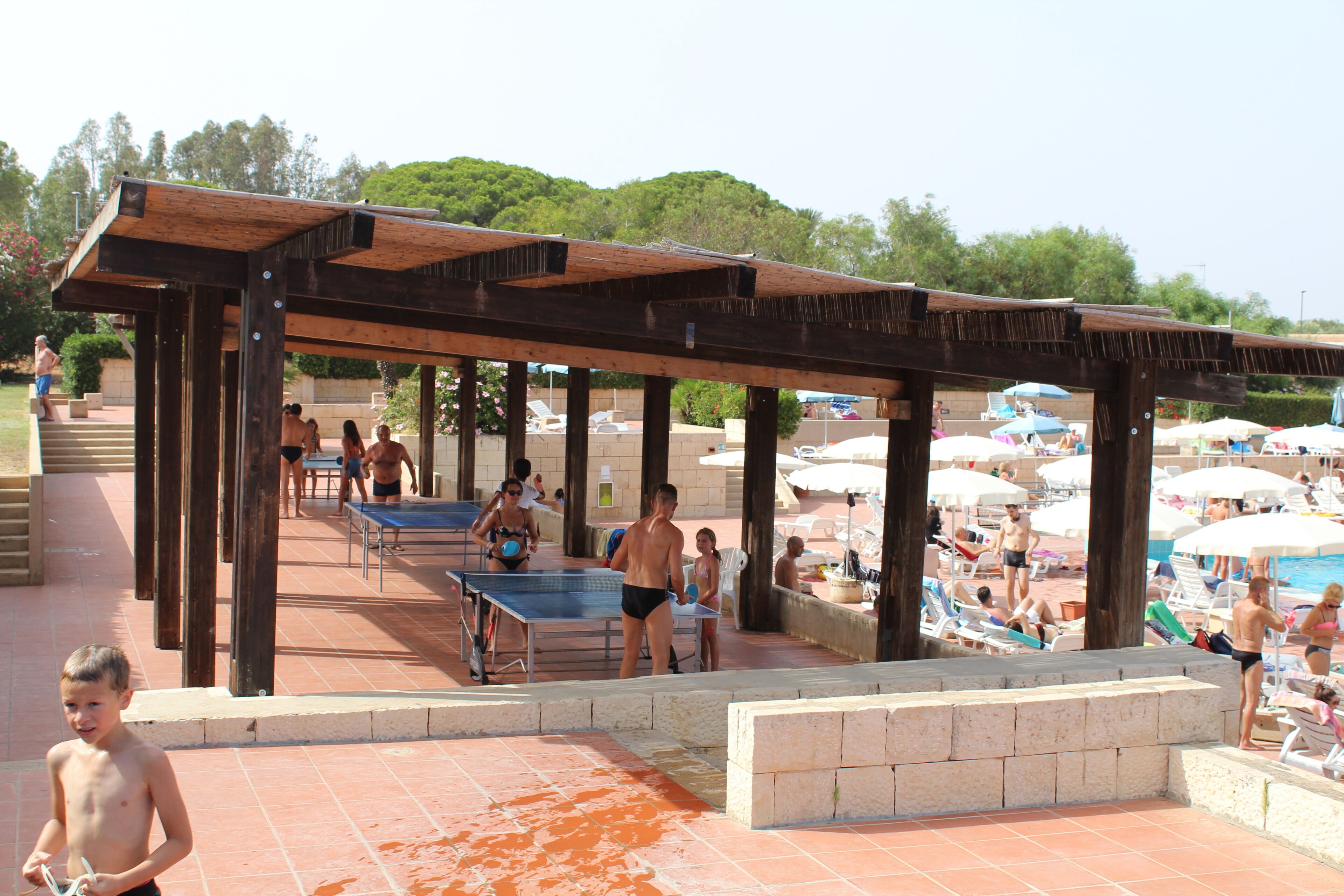 Ein Poolbereich im Freien mit einer Holzpergola, Liegestühlen und Sonnenschirmen.