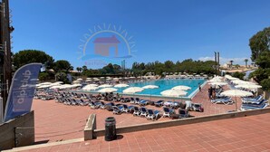 Ein Poolbereich mit Liegestühlen und Sonnenschirmen, ein klarer Himmel und eine Flagge mit dem Logo "Alpitour".