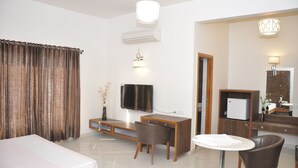 Habitació d'hotel amb llit, escriptori, cadira, televisió, mirall i taula petita.