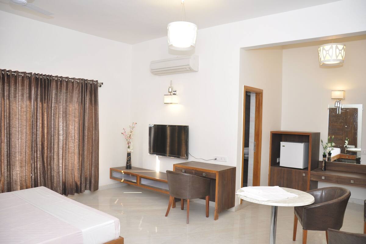 Una habitación de hotel con una cama, un escritorio, una silla, un televisor, un espejo y una mesita.