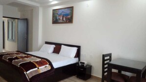 A bedroom with a bed, bedside table, and a desk with a chair. - S L Residency (Dhari)