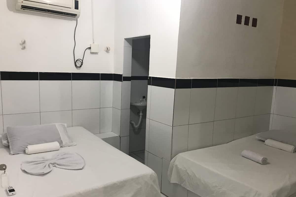 A hotel room with two beds, a small sink, and an air conditioning unit on the wall.