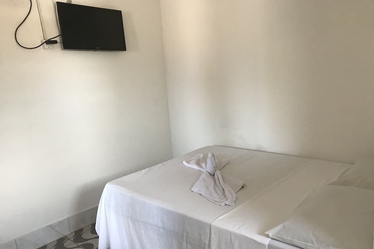 A neatly made bed with white linens and a folded towel, a flat-screen TV mounted on the wall, and a patterned floor.