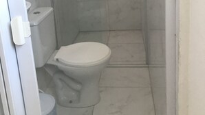 Un baño pequeño y cerrado con inodoro, cabina de ducha y puerta de cristal.