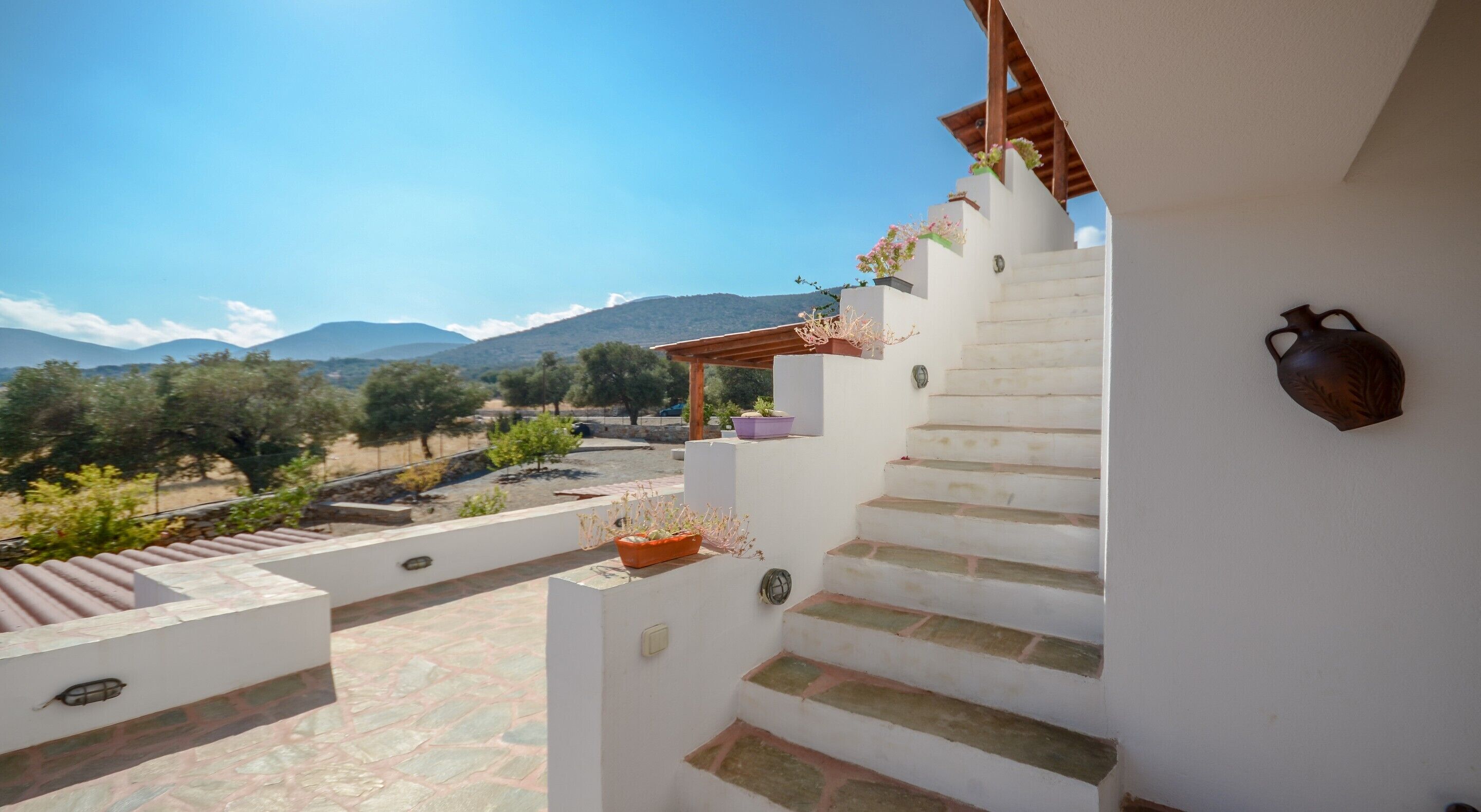 A white staircase leading to a terrace with potted plants and a view of mountains.