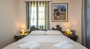 Une chambre d’hôtel avec un grand lit, deux tables de chevet avec des lampes, une fenêtre avec des rideaux et un tableau encadré au mur.