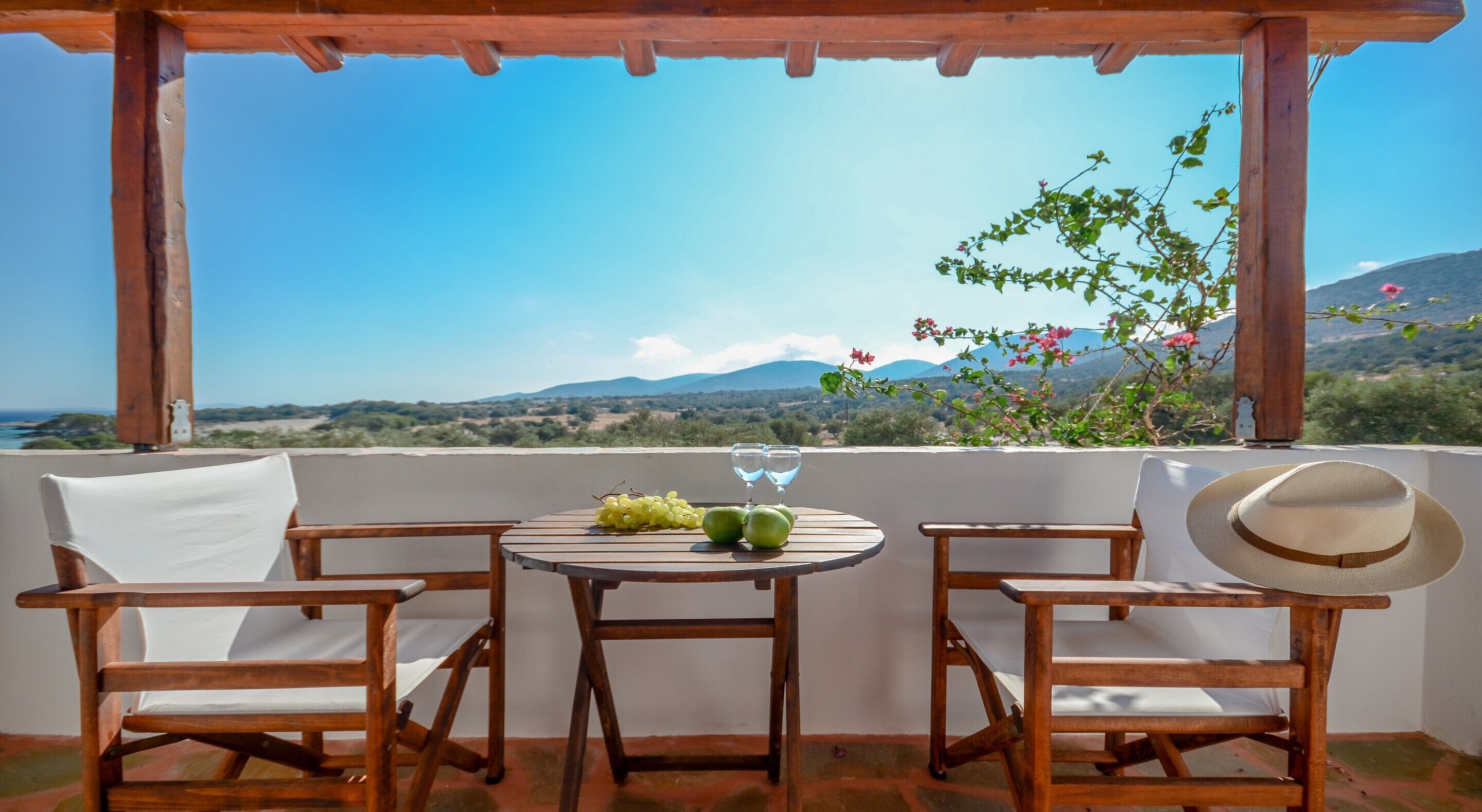 A wooden table with two chairs, a bottle of water, and a hat on the balcony overlooking a scenic landscape.