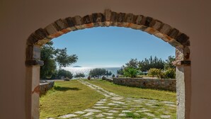 An arched doorway leading to a stone pathway and a grassy area with a view of the sea and distant land. - Theonis Villas, 30 meters from the beach (Naxos)