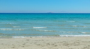 Une plage bordée d’une eau turquoise et cristalline, avec une montagne qui se profile à l’horizon.