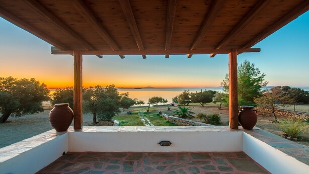 A covered outdoor area with a view of the sea at sunset, stone flooring, and two large vases. - Theonis Villas, 30 meters from the beach (Naxos)