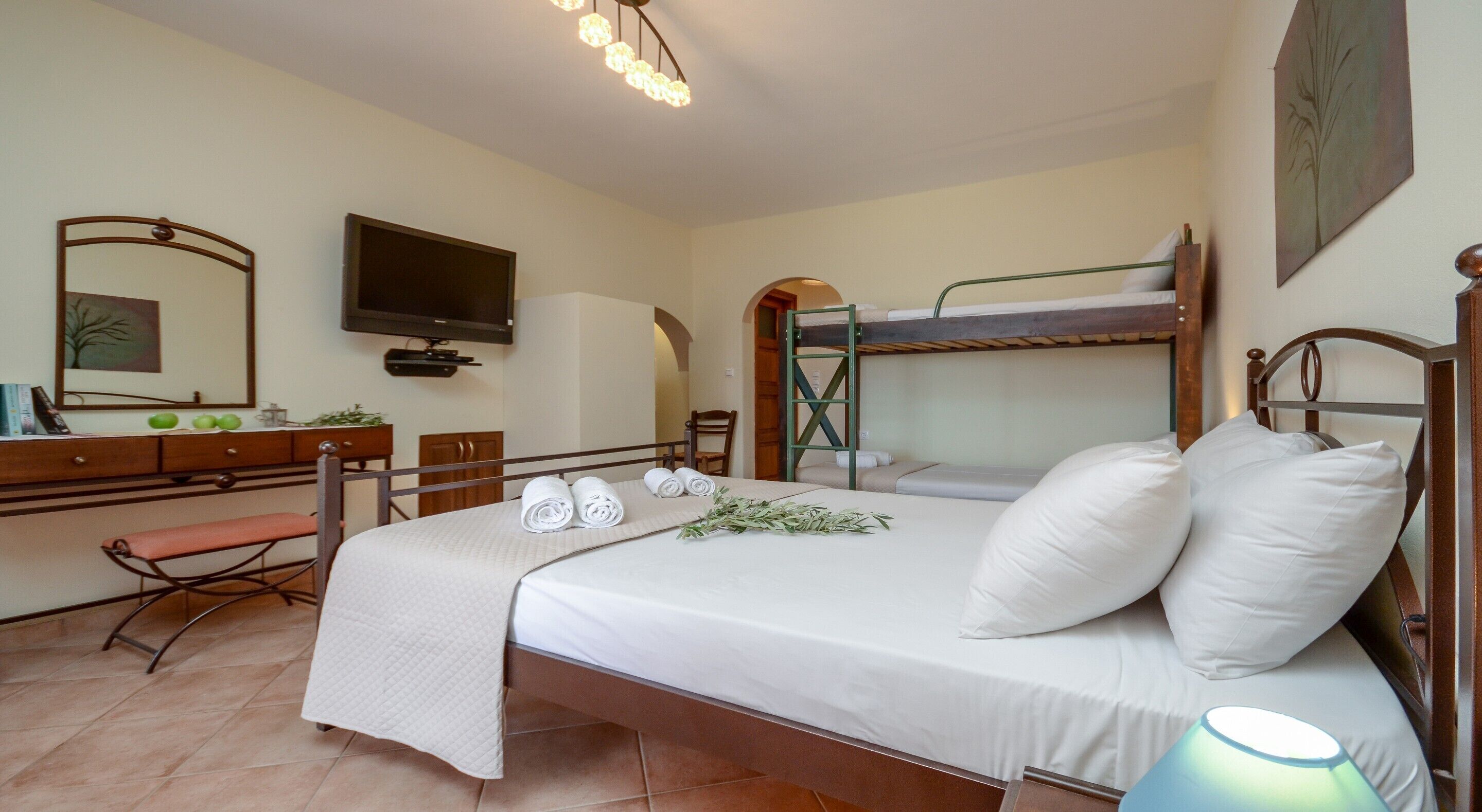 A bedroom with a bunk bed, a desk with a mirror, a television, and a bedside lamp.