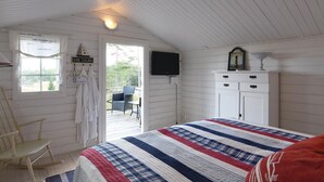 A bedroom with a bed, a television, a dresser, and a window with a view of the outdoors.