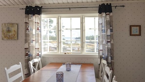 A dining area with a wooden table, white chairs, a window with curtains, and a view of a landscape.