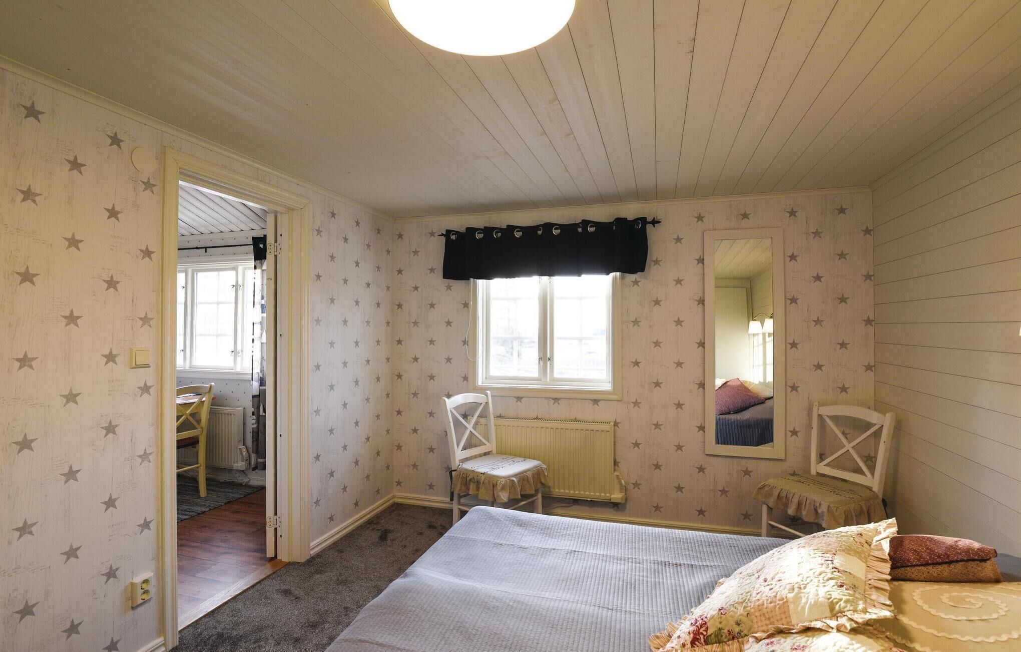 Een slaapkamer met een bed, twee stoelen, een raam met gordijn, een radiator en een deur naar een andere kamer.
