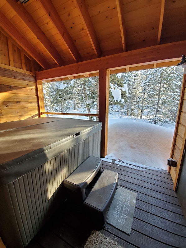 Relax in a hot tub on a deck with a serene view of the surrounding trees.