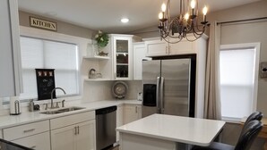 A modern kitchen with white cabinetry, a stainless steel refrigerator, a built-in dishwasher, and a chandelier.