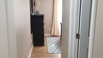 A narrow hallway with wooden flooring, a black cabinet, a patterned rug, and a door with a metal handle.