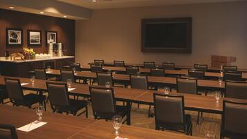 A conference room with multiple tables and chairs, a buffet area with fruits and beverages, and a large screen on the wall.