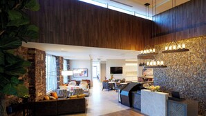 Un hall d’entrée spacieux avec un plafond haut, un mur décoratif en pierre, un comptoir de réception et un espace détente avec un canapé et une table basse.