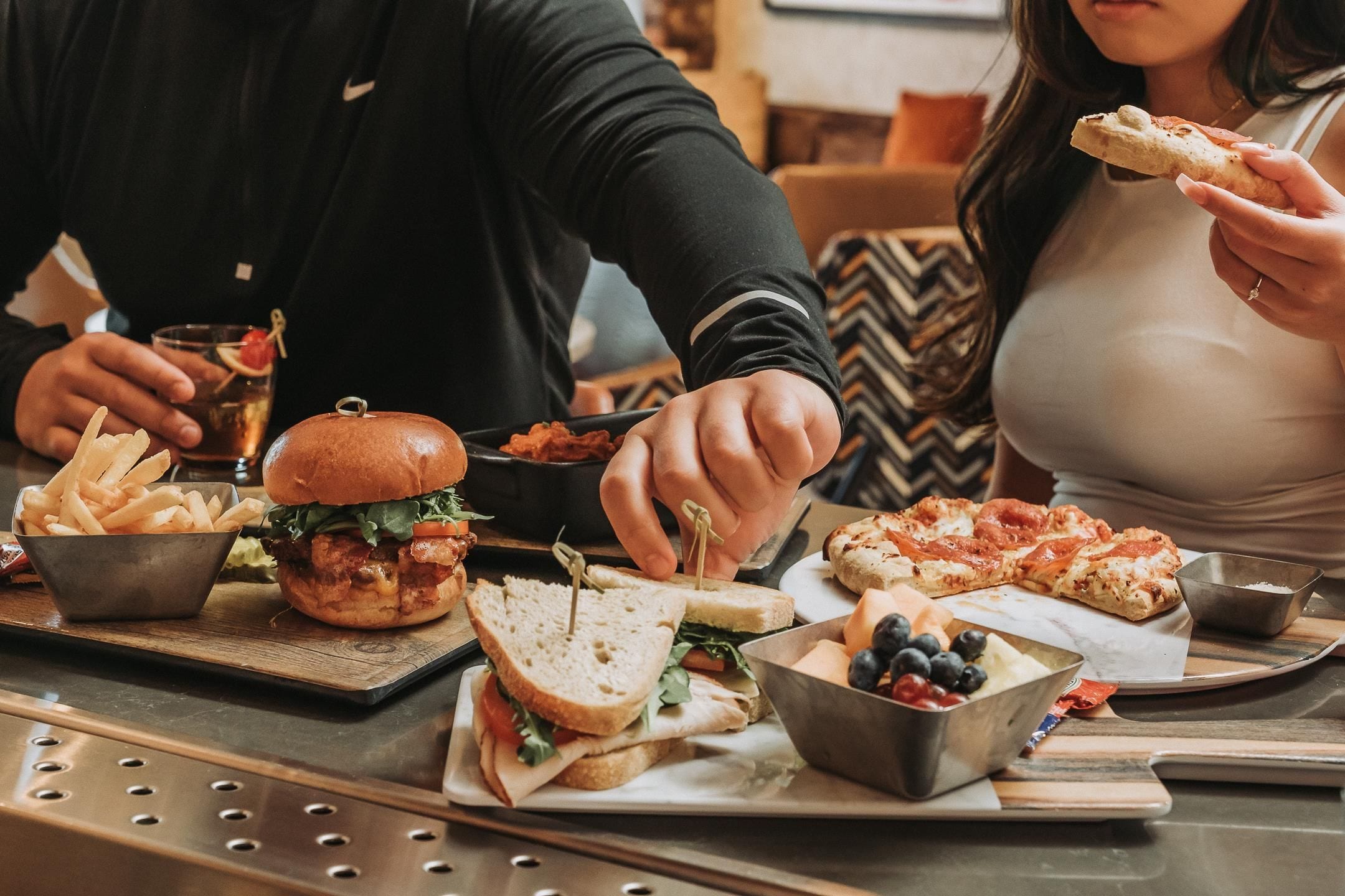 Una mesa de comedor con comida que incluye una hamburguesa, sándwiches, papas fritas y una pizza.