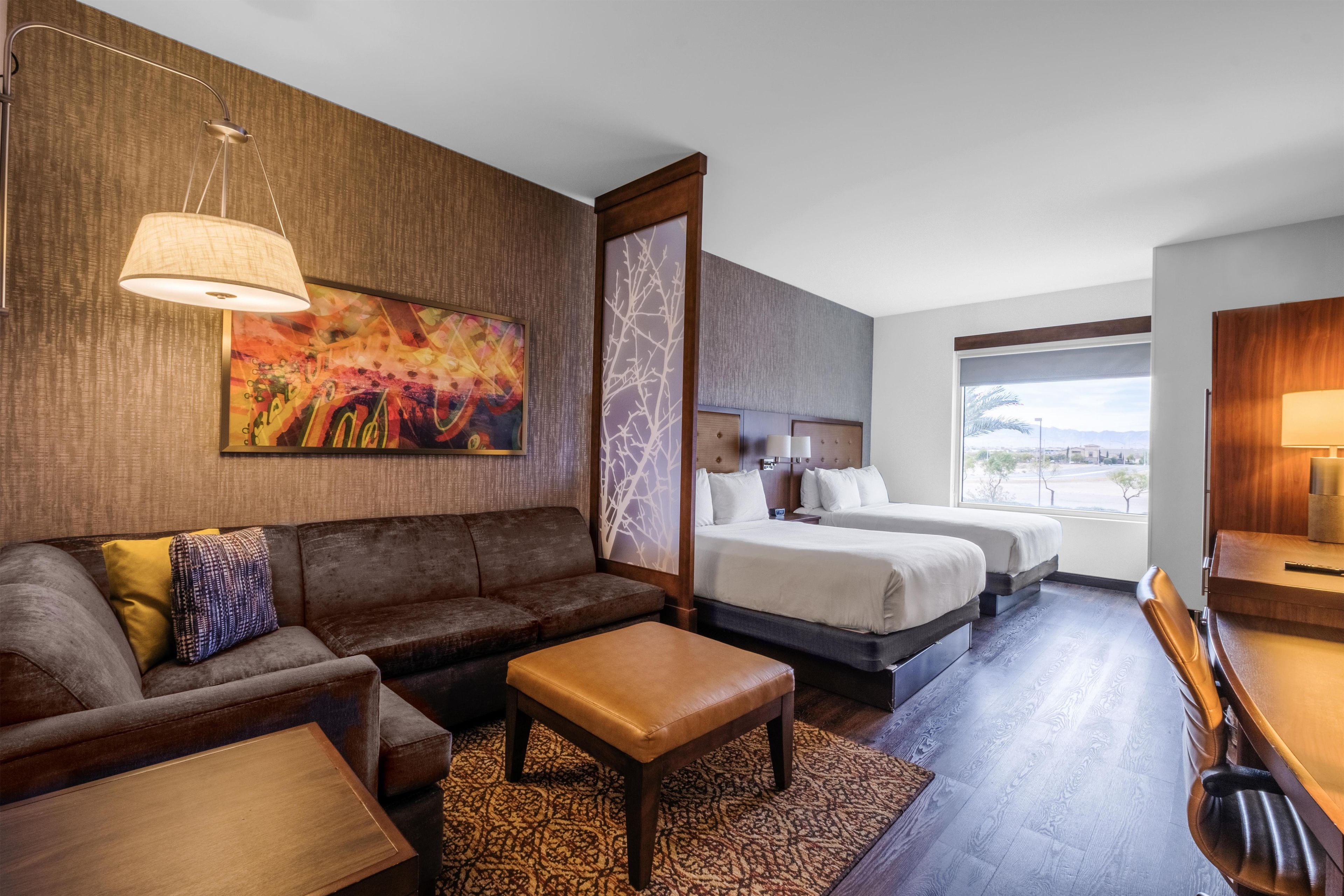 A hotel room with a sofa, a bed, a desk, and a large window.