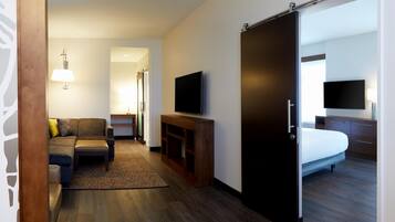 Ein Hotelzimmer mit einer Couch, einem Fernseher, einem Bett und einer Schiebetür.
