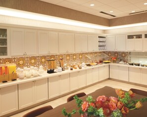 Een hotelkeuken met witte kasten, een decoratieve achterwand en een buffet met verschillende soorten eten.