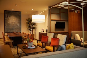 Un hall d’hôtel moderne comprenant un espace repas, des coins salon, une grande œuvre d’art et un téléviseur.