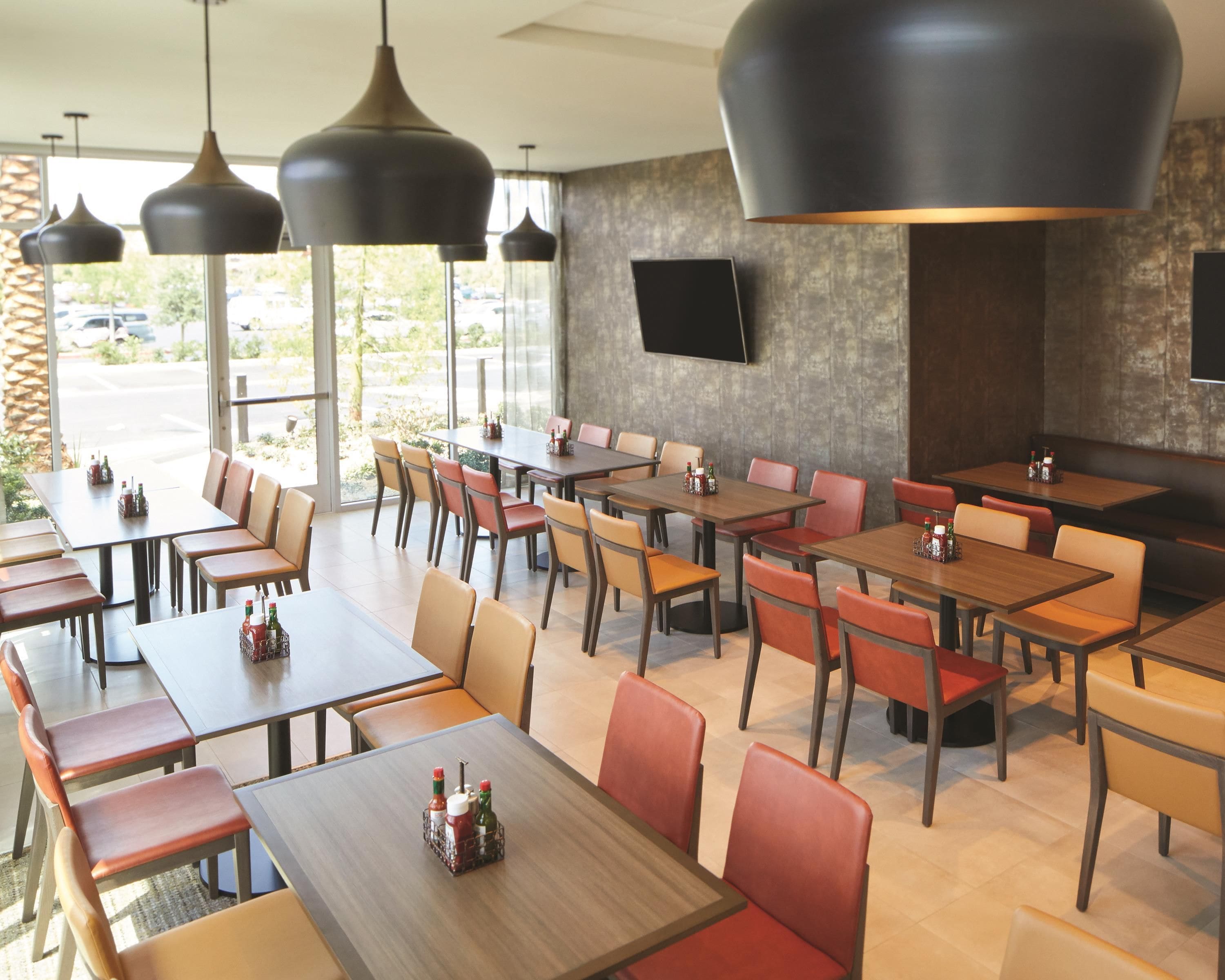 A restaurant with multiple tables and chairs, a flat-screen TV mounted on the wall, and pendant lighting.