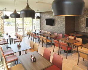 Un restaurant doté de nombreuses tables et chaises, d’un téléviseur à écran plat fixé au mur et d’un éclairage suspendu.