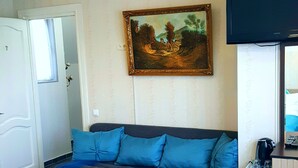 A living room with a sofa, a coffee table, a painting, and a television. - Hotel Antalia (Tbilisi)