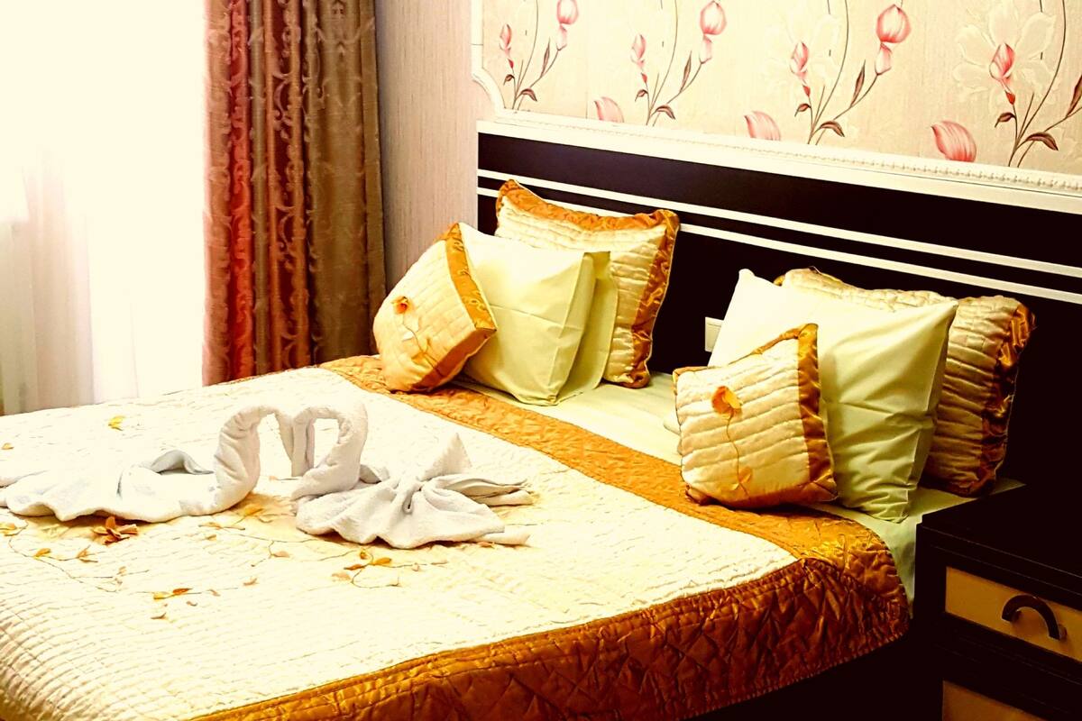A bedroom with a bed, pillows, a nightstand, and a wall with floral wallpaper.