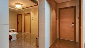 A hallway with marble flooring, wooden doors, and a small table with a chair. - Hotel Leela (Kalyan)