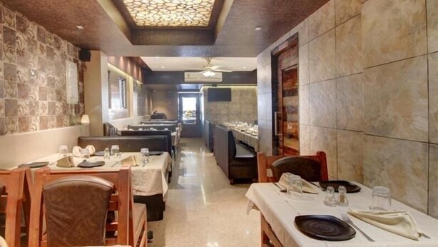 A restaurant with a long counter, multiple tables, and booths. - Hotel Leela (Kalyan)
