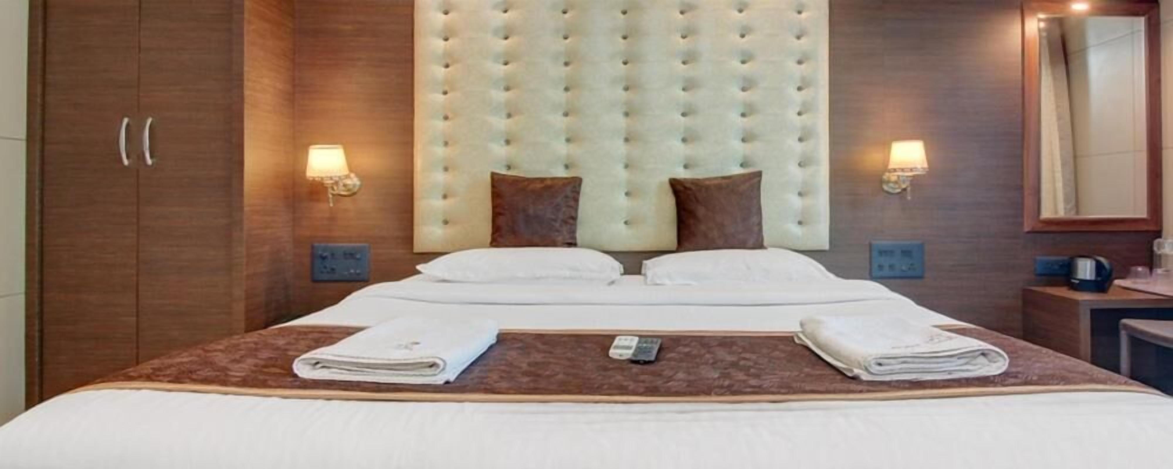 A hotel room with a large bed, two bedside tables, a wooden wardrobe, and wall-mounted lamps.