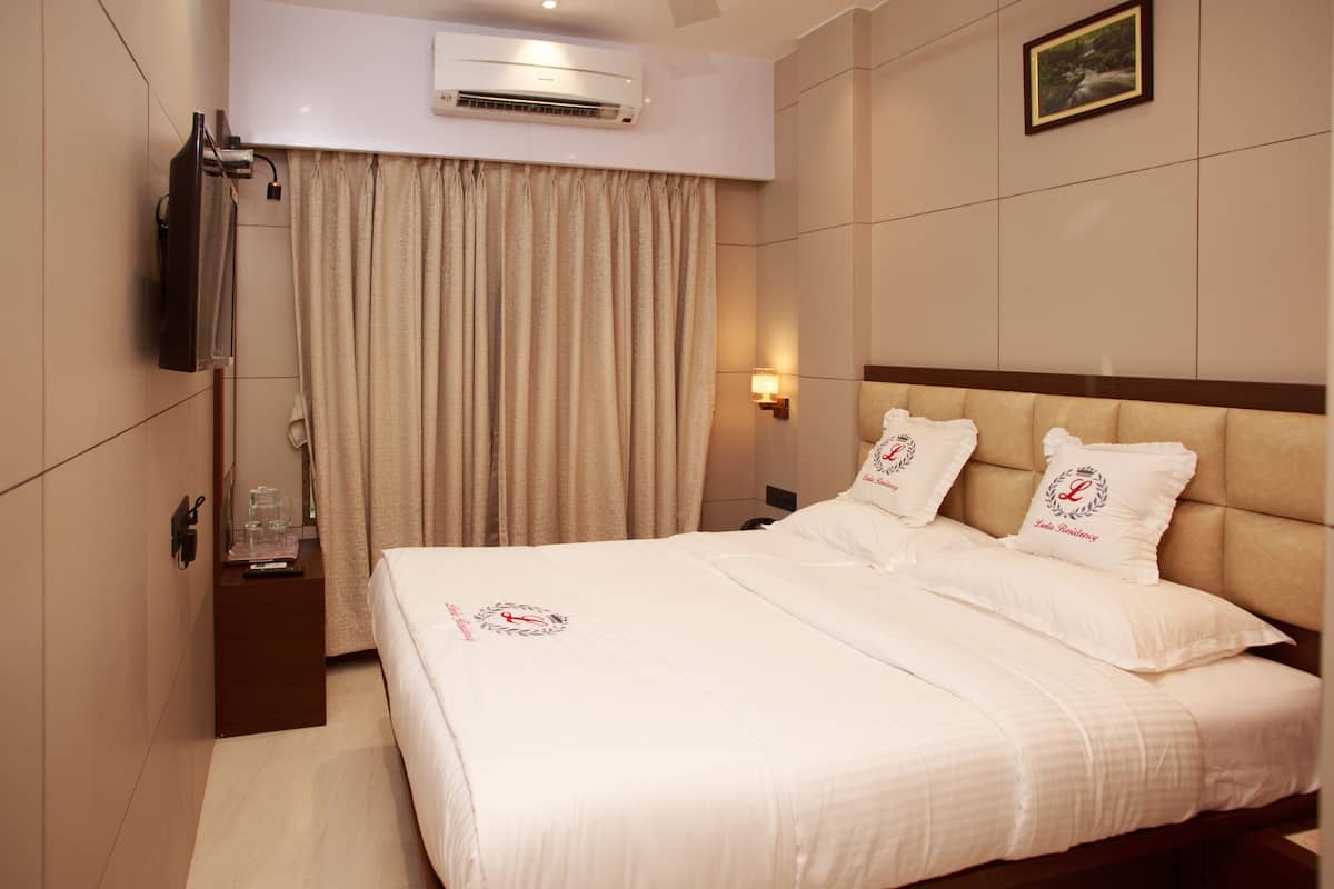 A hotel room with a large bed, a bedside table with a glass of water, a TV mounted on the wall, and a curtain.