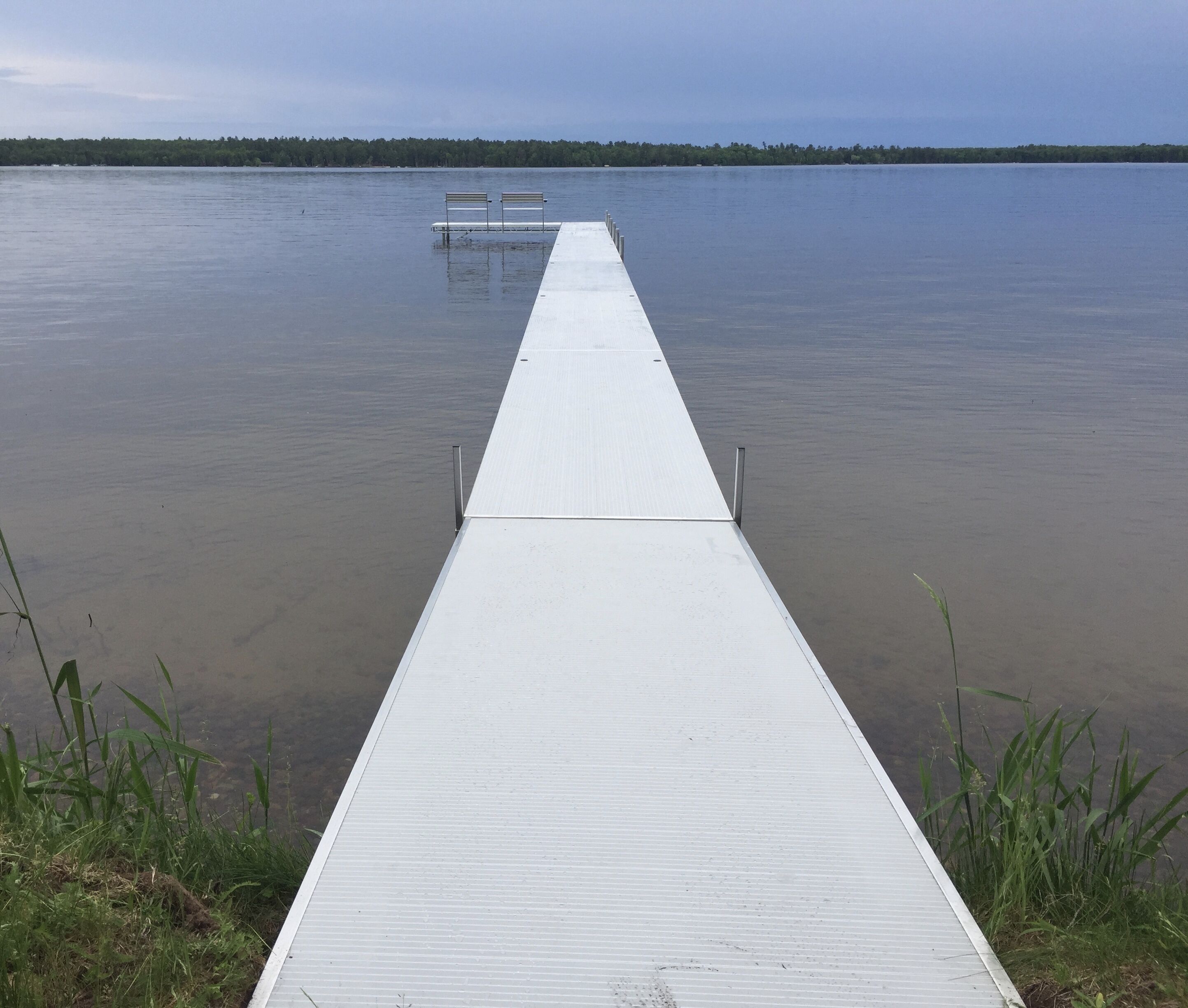 A long, narrow wooden dock extending into calm water, with two benches at the end.