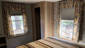 Un dormitorio con una cama, dos ventanas con cortinas, una puerta de madera y una estantería.